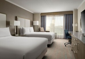 Two spacious beds with white linens, bedside tables, and lamps, plus a desk, chair, and flat-screen TV.