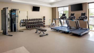 A gym with treadmills, weight machines, and a wall of dumbbells.
