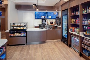 A coffee shop with a menu board, a coffee machine, a refrigerator, and shelves stocked with snacks and beverages. - DoubleTree by Hilton Irvine - Spectrum (Irvine)