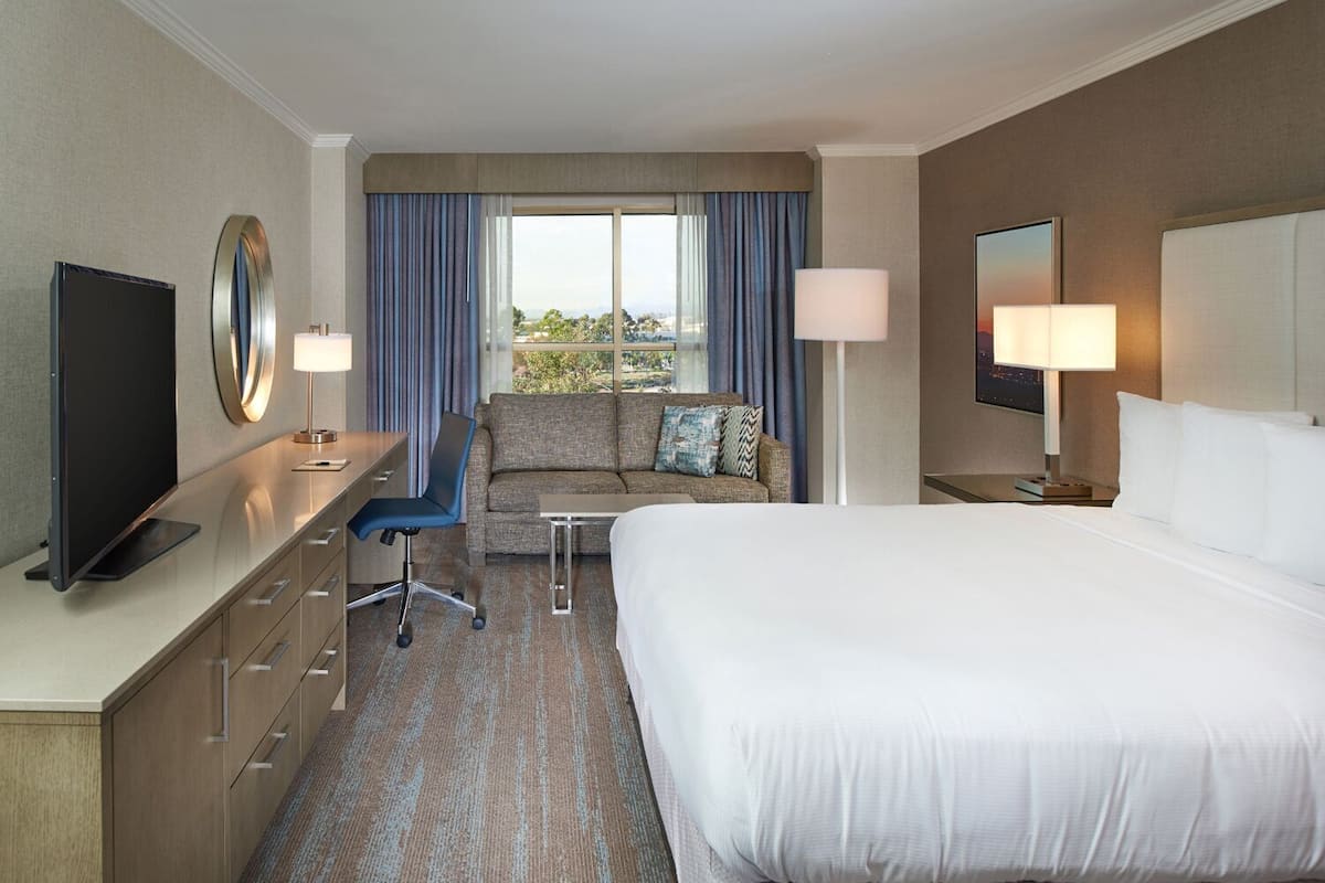 Una habitación de hotel con cama, escritorio, silla, televisión y vistas al exterior.