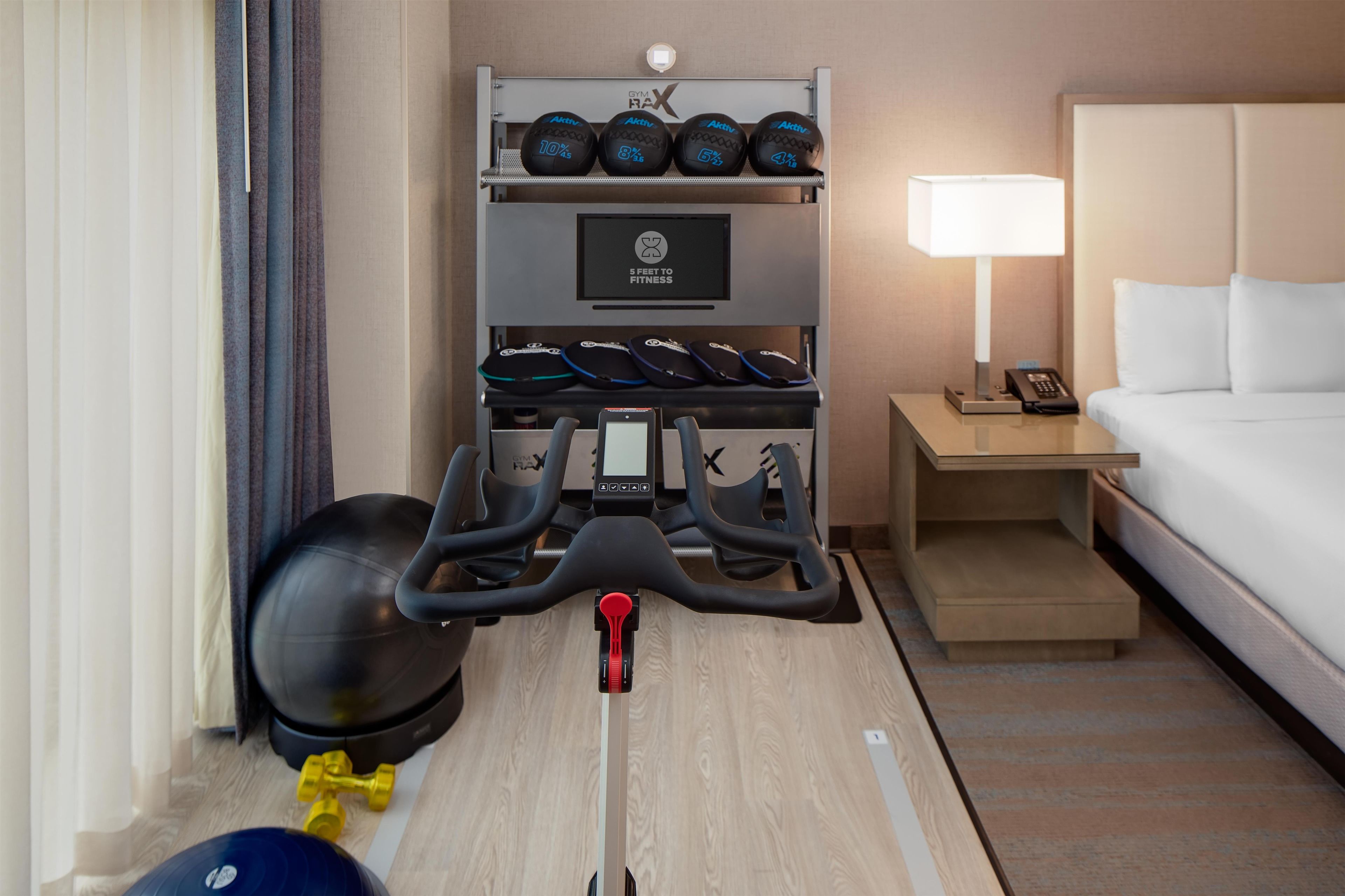 A hotel room with a treadmill, exercise balls, and a bed.