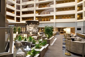 Eine mehrstöckige Hotelhalle mit einer zentralen Fontäne, Sitzbereichen und einem großen Wandgemälde.