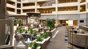 Un hall d’hôtel à plusieurs niveaux, doté d’une fontaine centrale, de coins salon et d’un grand écran.