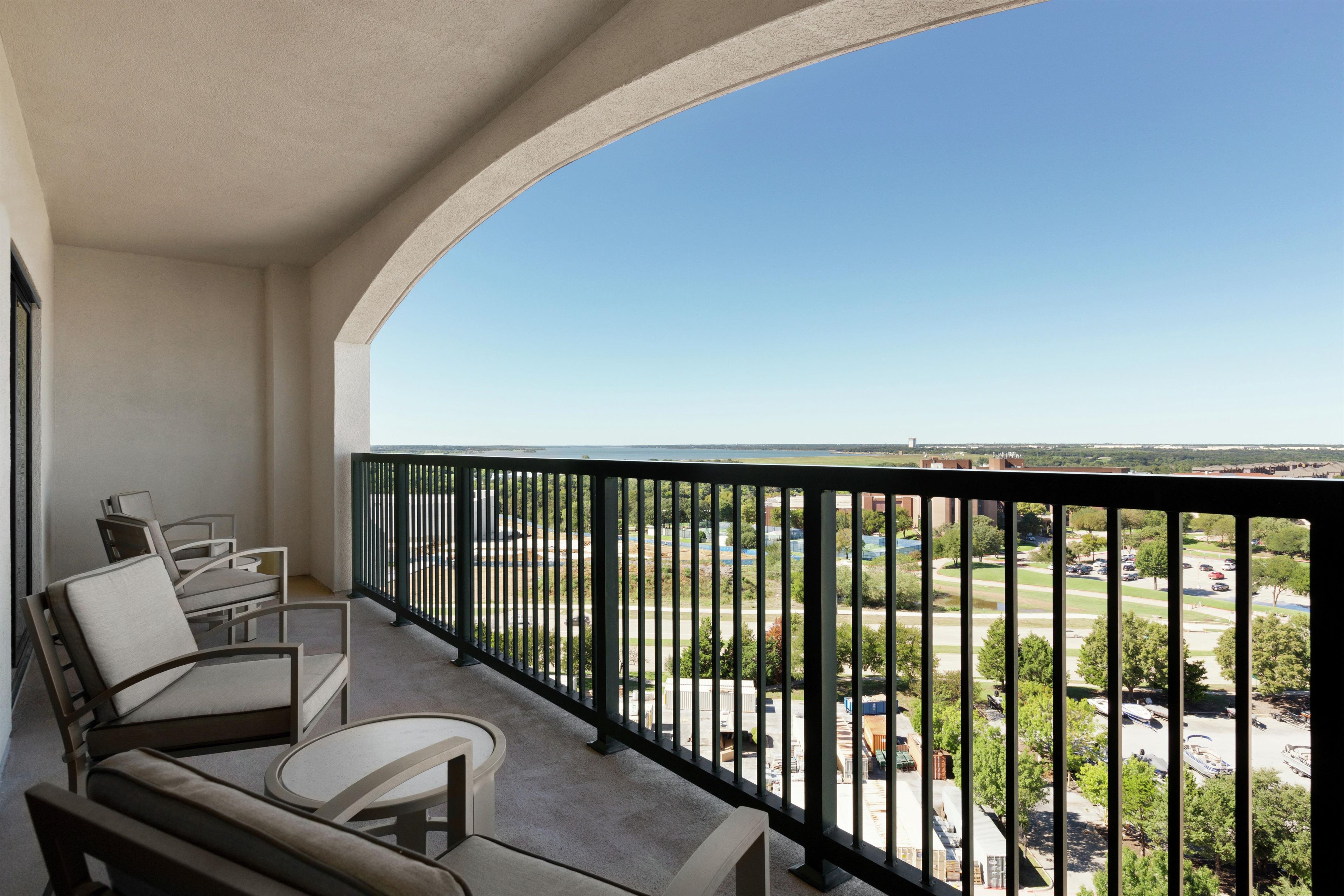 A balcony with a view of a parking lot and buildings.