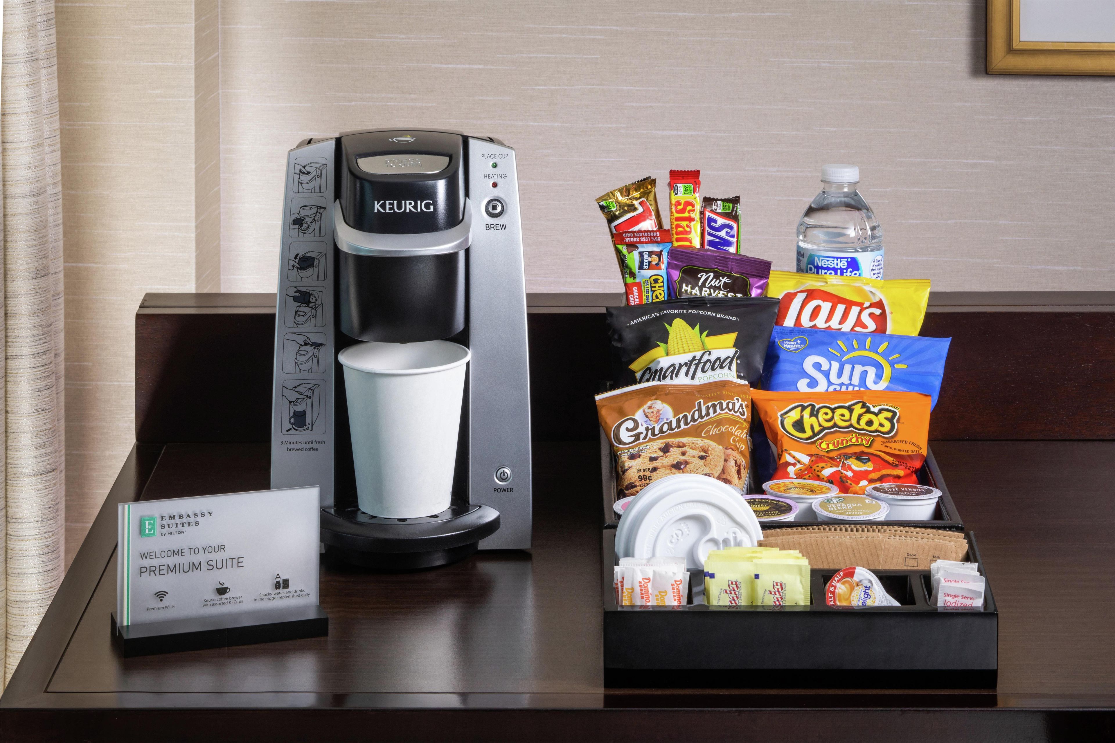 A coffee maker and a tray of snacks and beverages on a hotel counter.