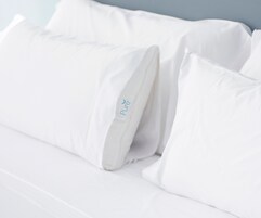 Una cama blanca con almohadas, una de ellas con la etiqueta que dice "Pure".