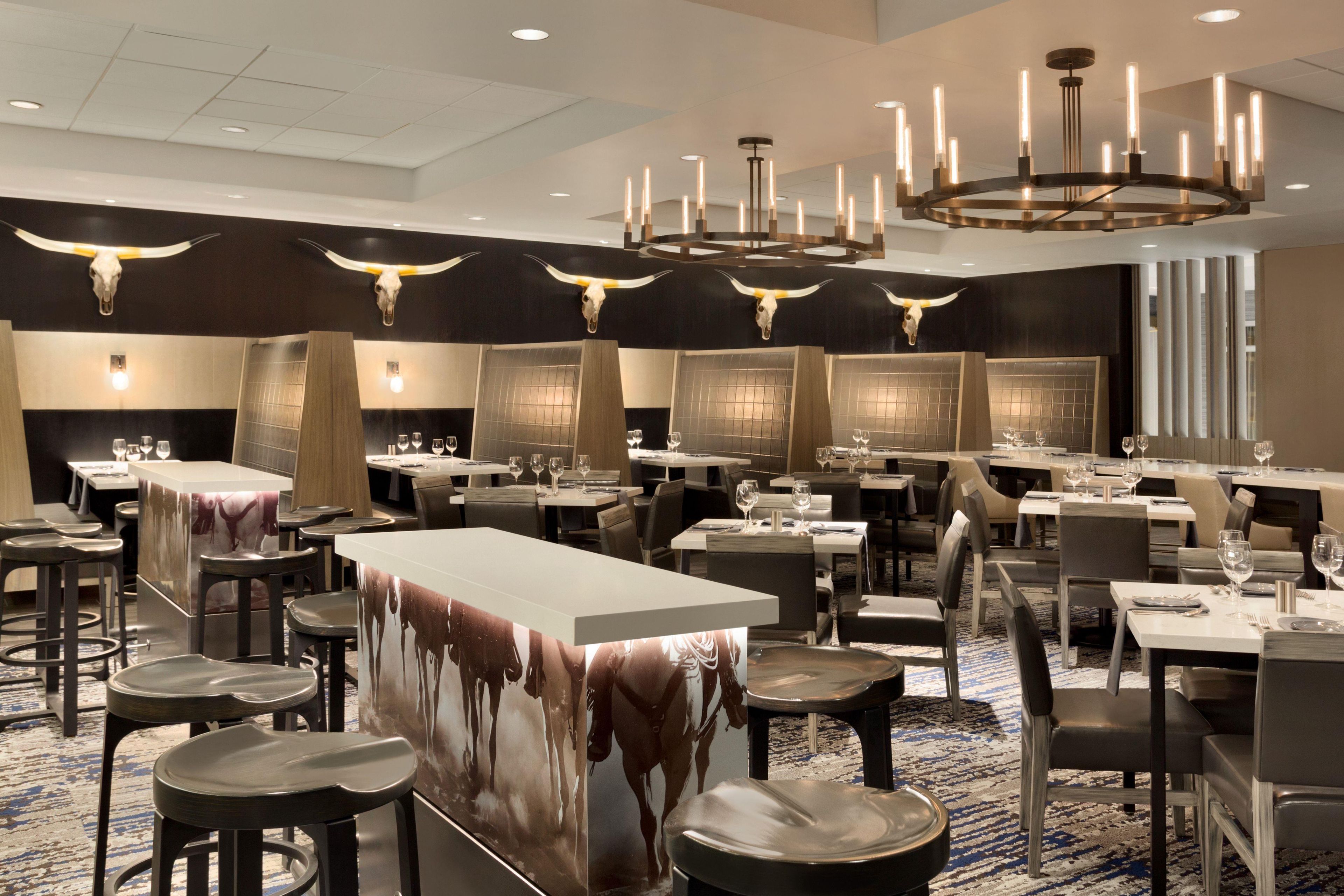 En restaurant med flere borde og stole, et barområde og et loft med hængende lamper.