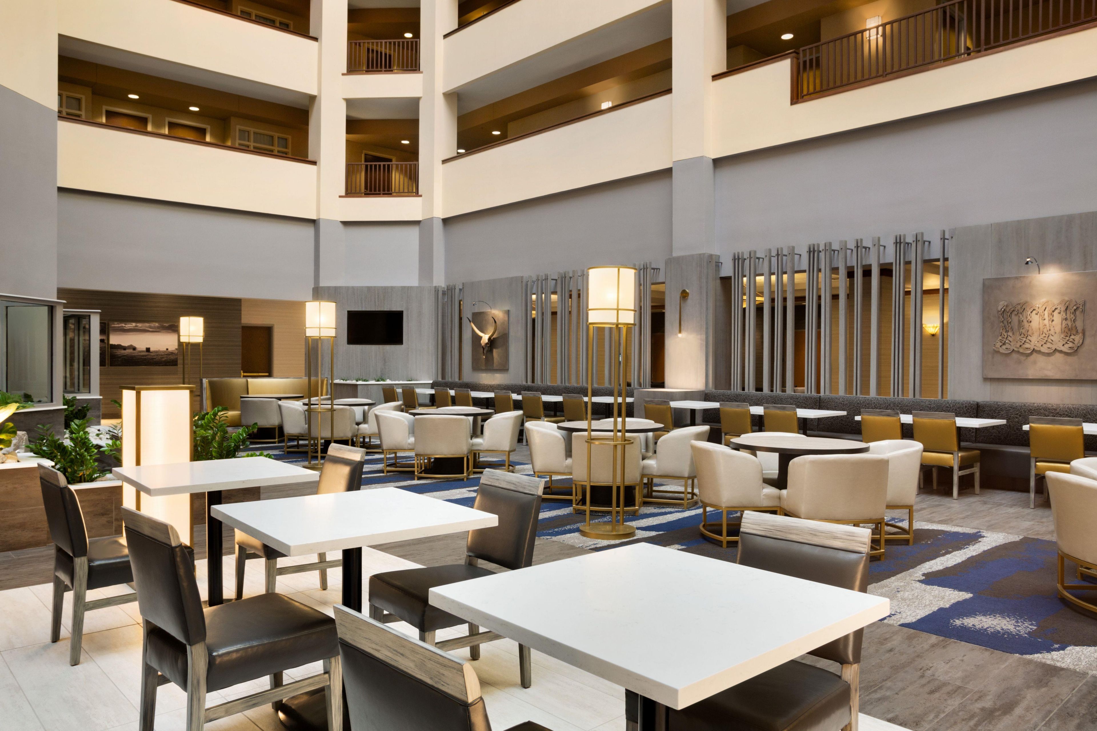 A spacious hotel lobby with multiple dining areas, high ceilings, and modern decor.