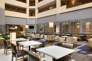 Un hall d’hôtel spacieux, doté de plusieurs espaces de restauration, de hauts plafonds et d’un décor moderne.