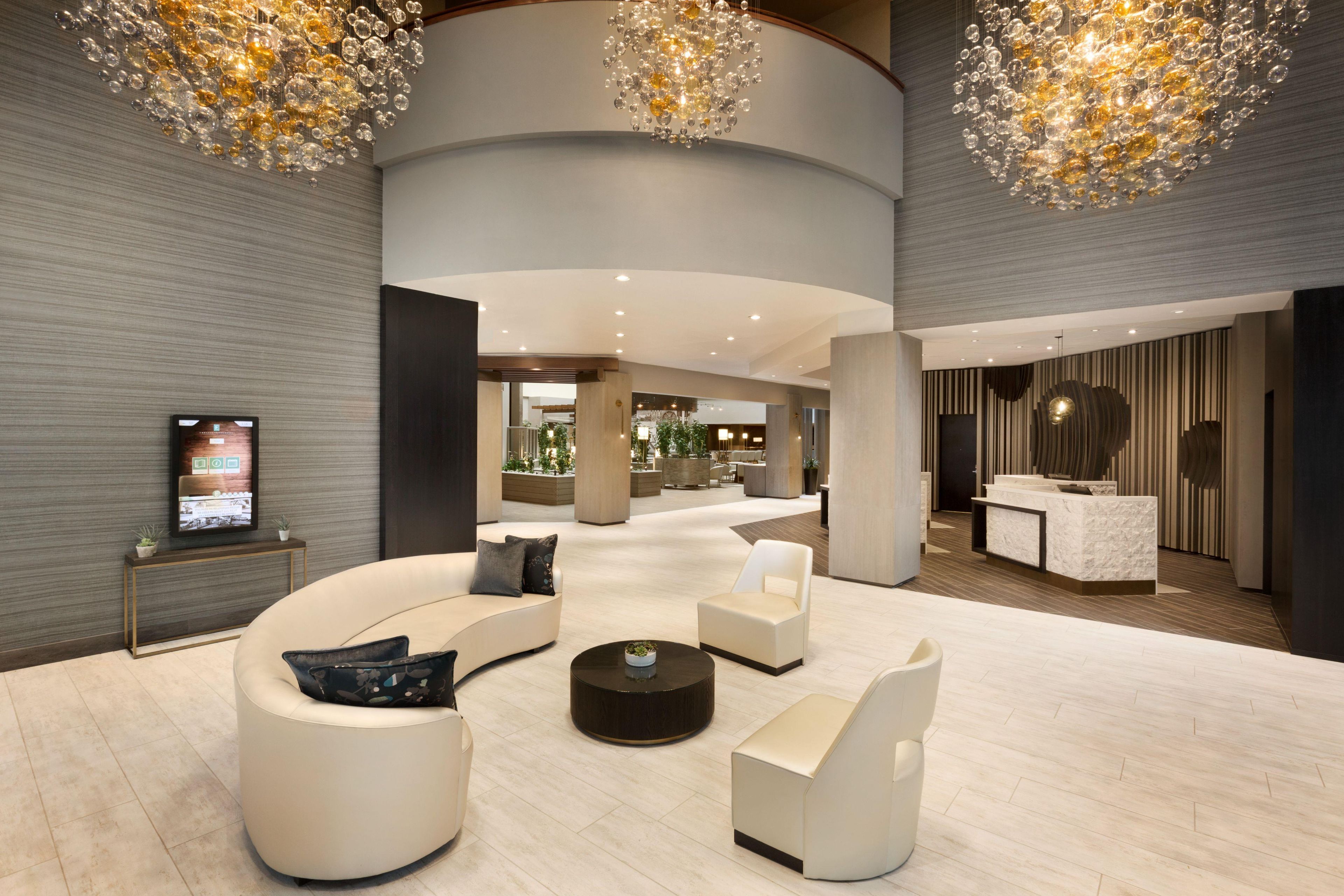 Un hall d’entrée moderne avec un espace salon aux lignes courbes, un comptoir d’accueil et un grand lustre.