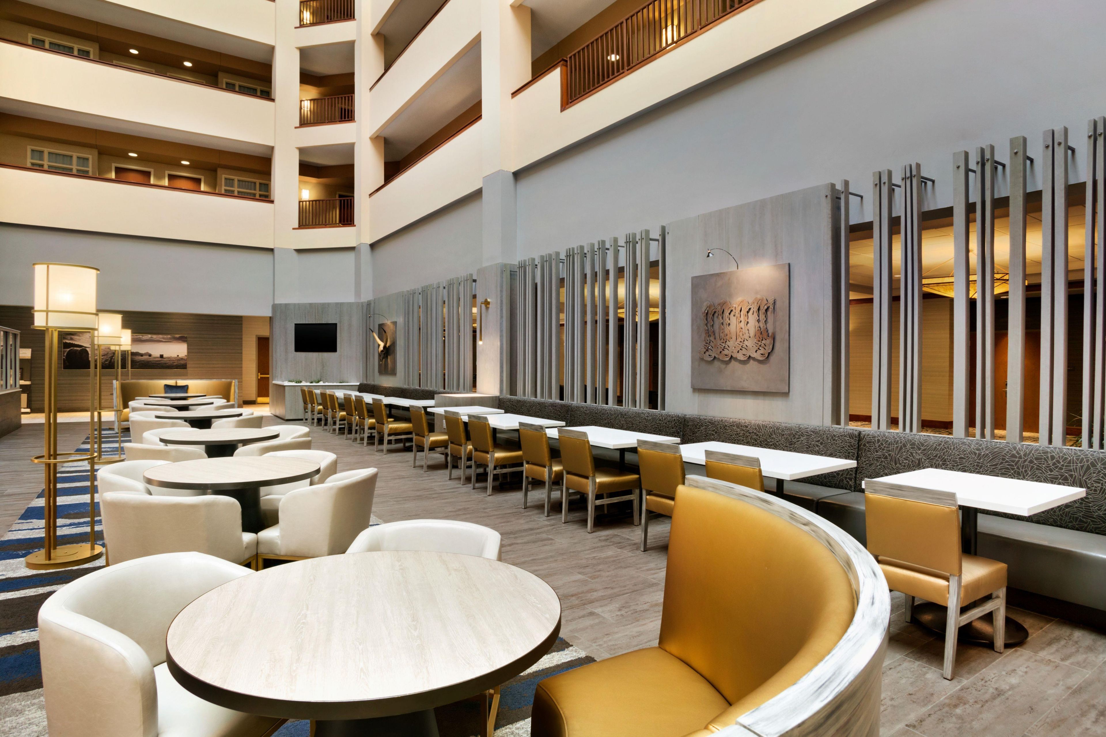 Un hall de hotel con varias zonas de comedor, incluidas mesas redondas y cabinas, y un techo alto de diseño moderno.