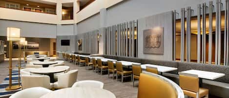 Un hall de hotel con varias zonas de comedor, incluidas mesas redondas y cabinas, y un techo alto de diseño moderno.