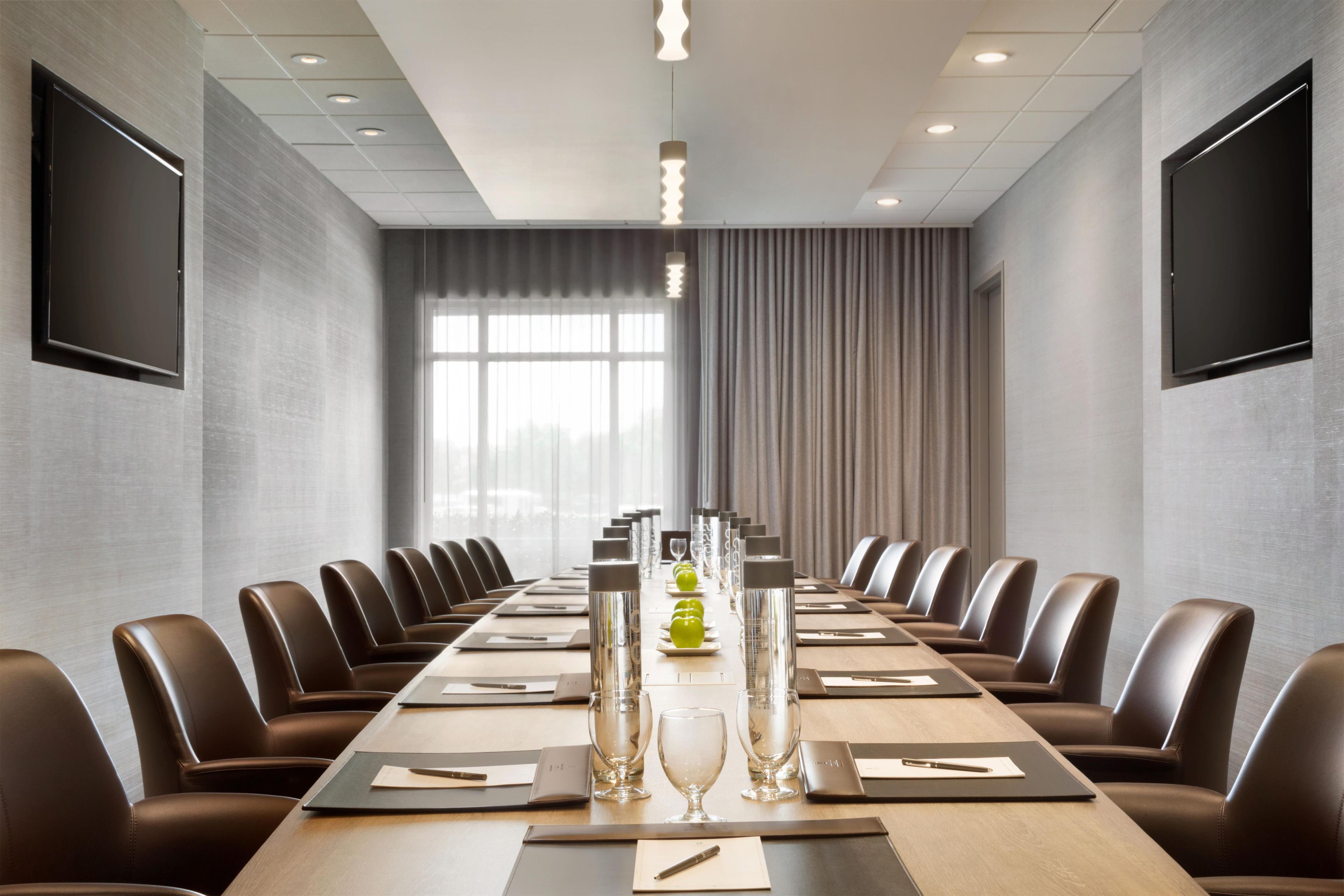 Une salle de conférence avec une longue table, des fauteuils en cuir et une grande fenêtre avec des rideaux.