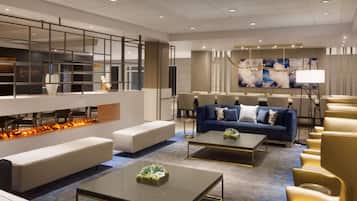 A modern hotel lobby with a seating area, a fireplace, and a dining setup.
