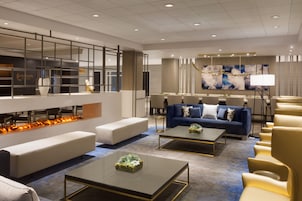 A modern hotel lobby with a seating area, a fireplace, and a dining setup.
