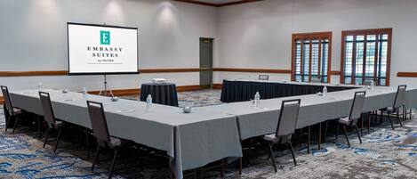 A conference room with a long table, chairs, a projector screen, and a carpeted floor.