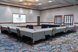 Una sala de conferencias con una larga mesa, sillas, una pantalla de proyector y piso alfombrado.