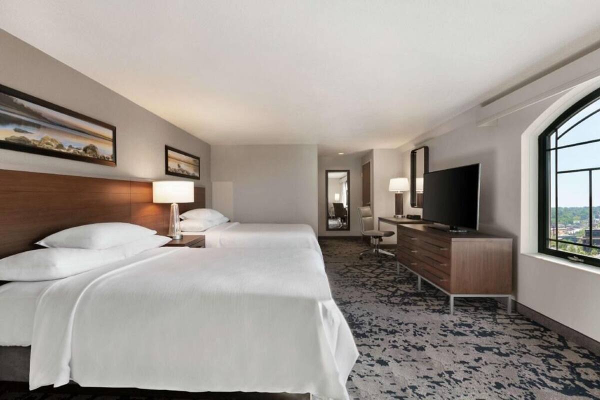 Een hotelkamer met twee bedden, een televisie, een bureau en een groot raam.