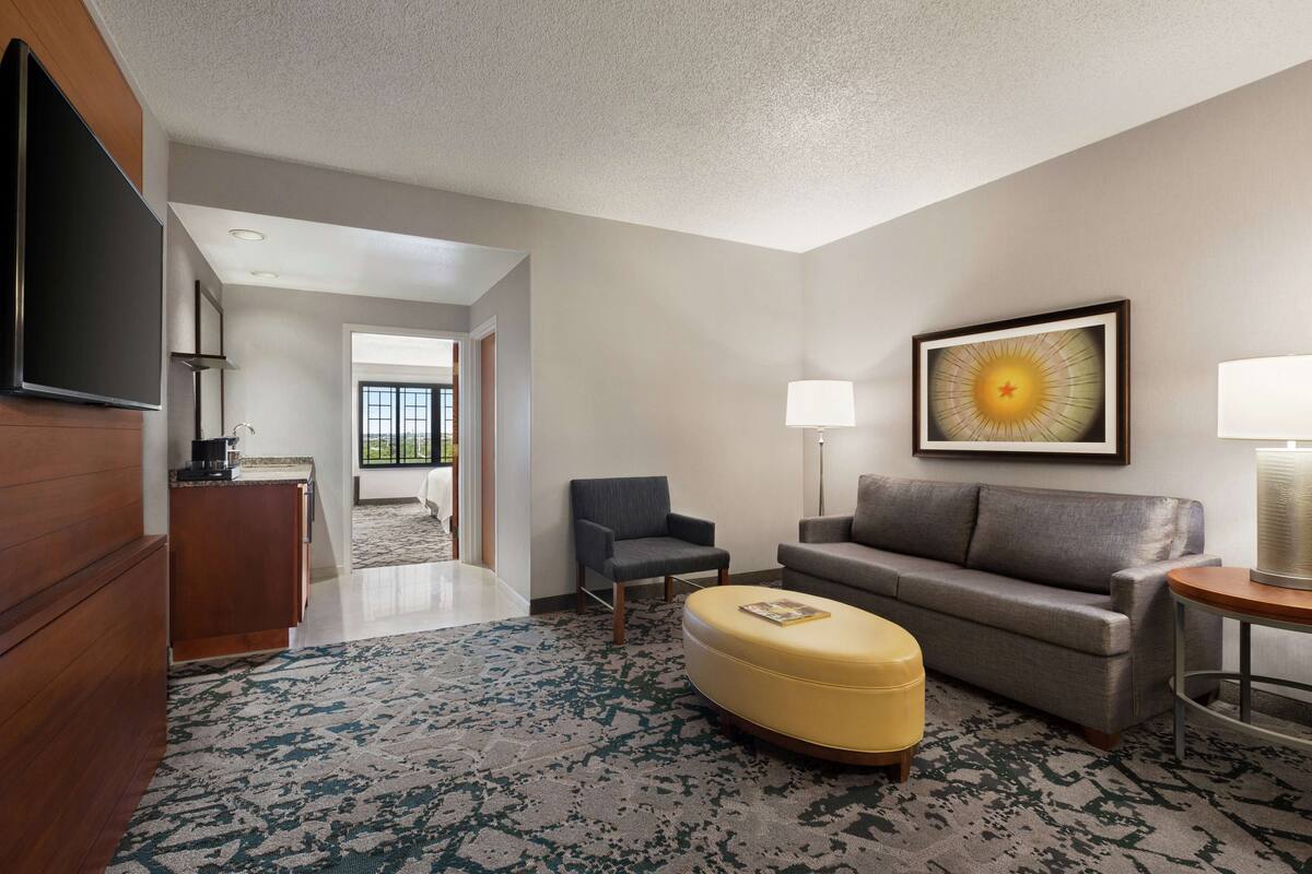 Een moderne hotelkamer met een flatscreen televisie, een bank, een stoel, een klein tafeltje en een decoratief wandobject.