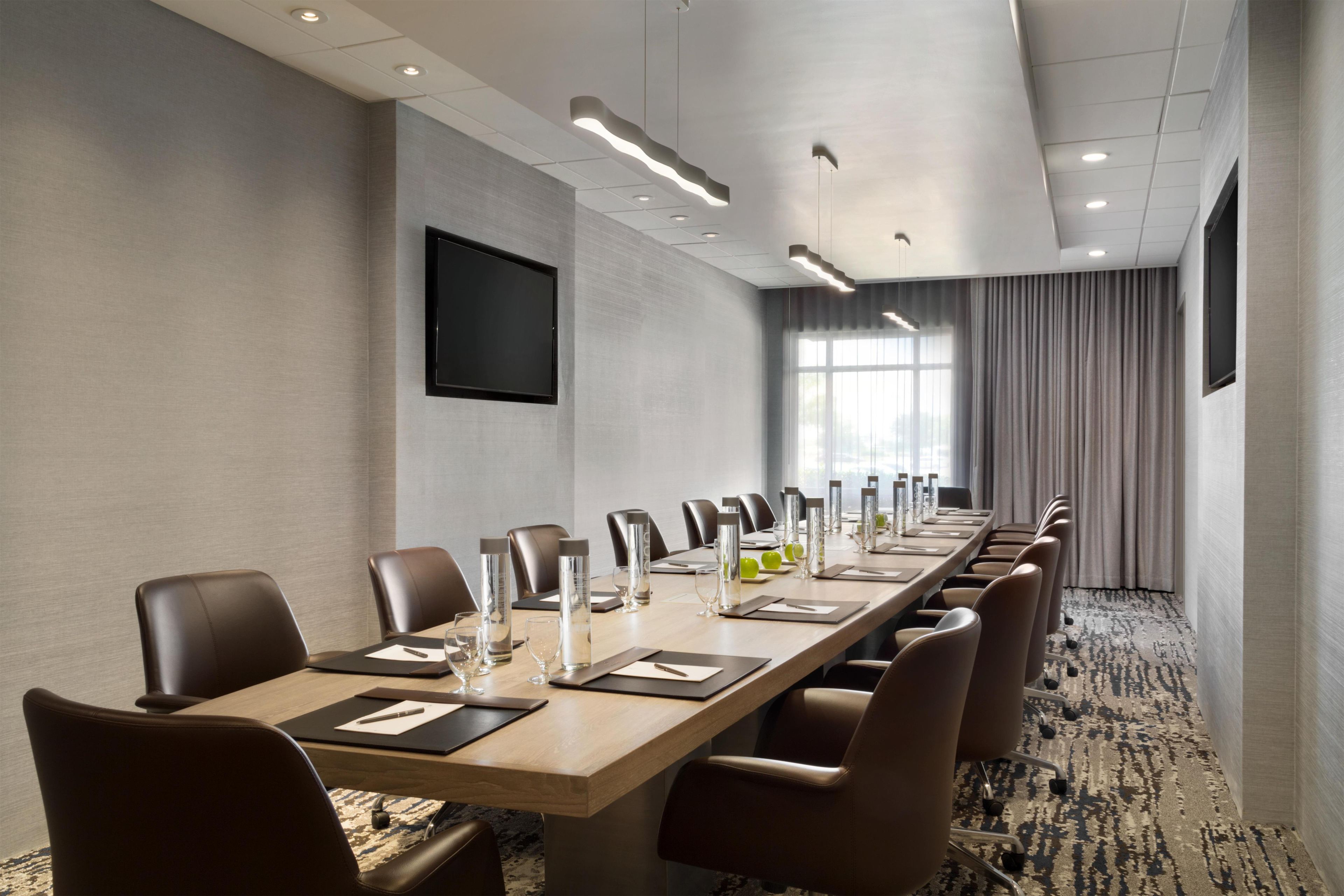 Une salle de conférence avec une longue table, des chaises et un téléviseur à écran plat fixé au mur.