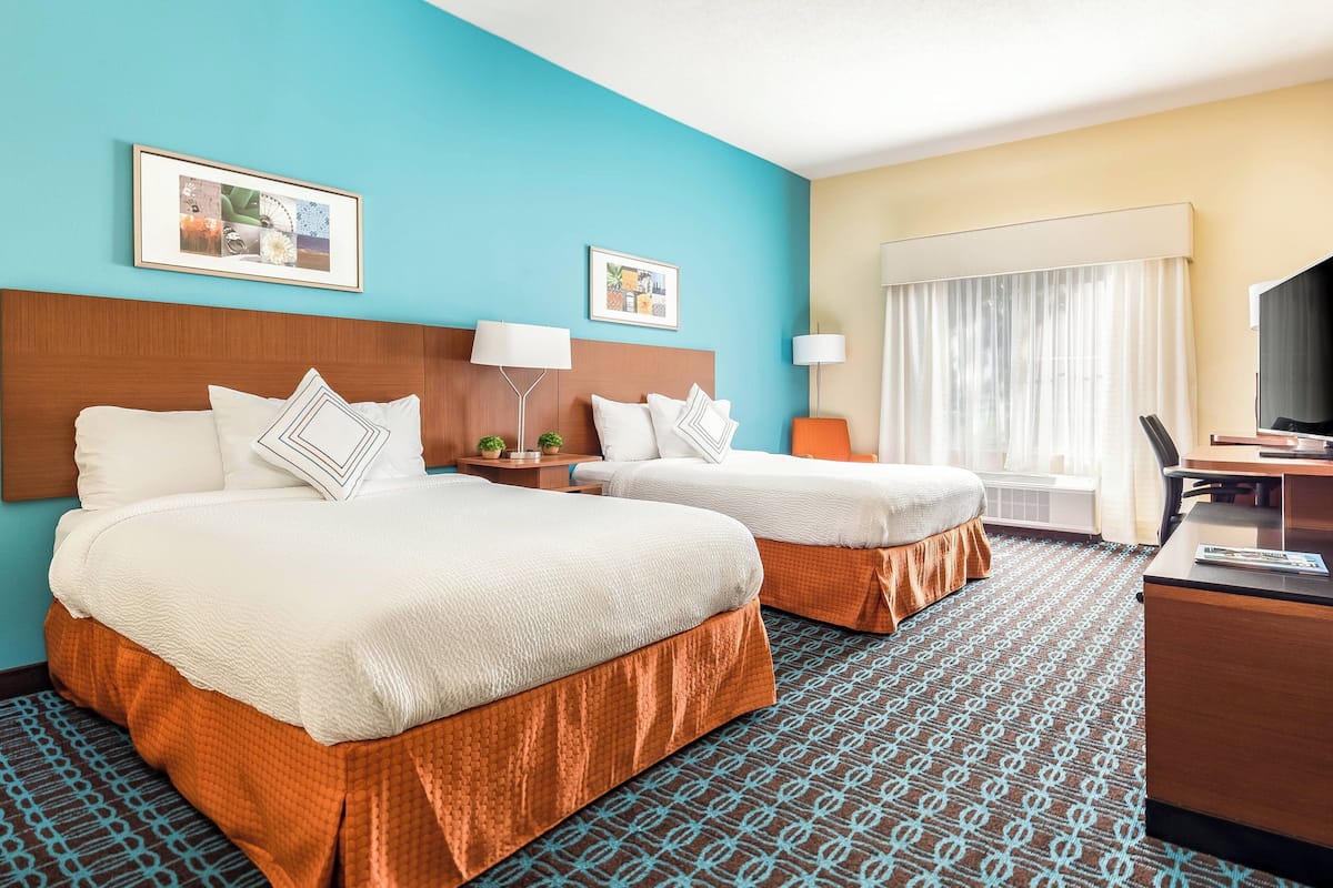 A hotel room with two beds, a desk, and a TV.