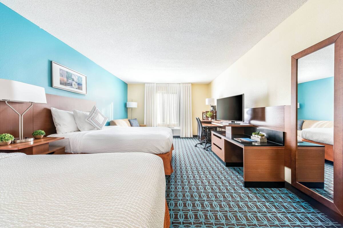 A hotel room with two beds, a desk, a TV, and a large mirror.