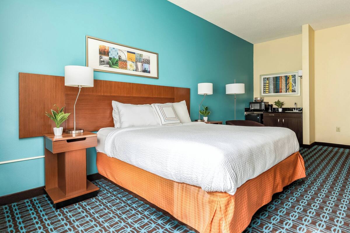 A hotel room with a large bed, two bedside tables with lamps, a small desk with a microwave, and a wall-mounted TV.