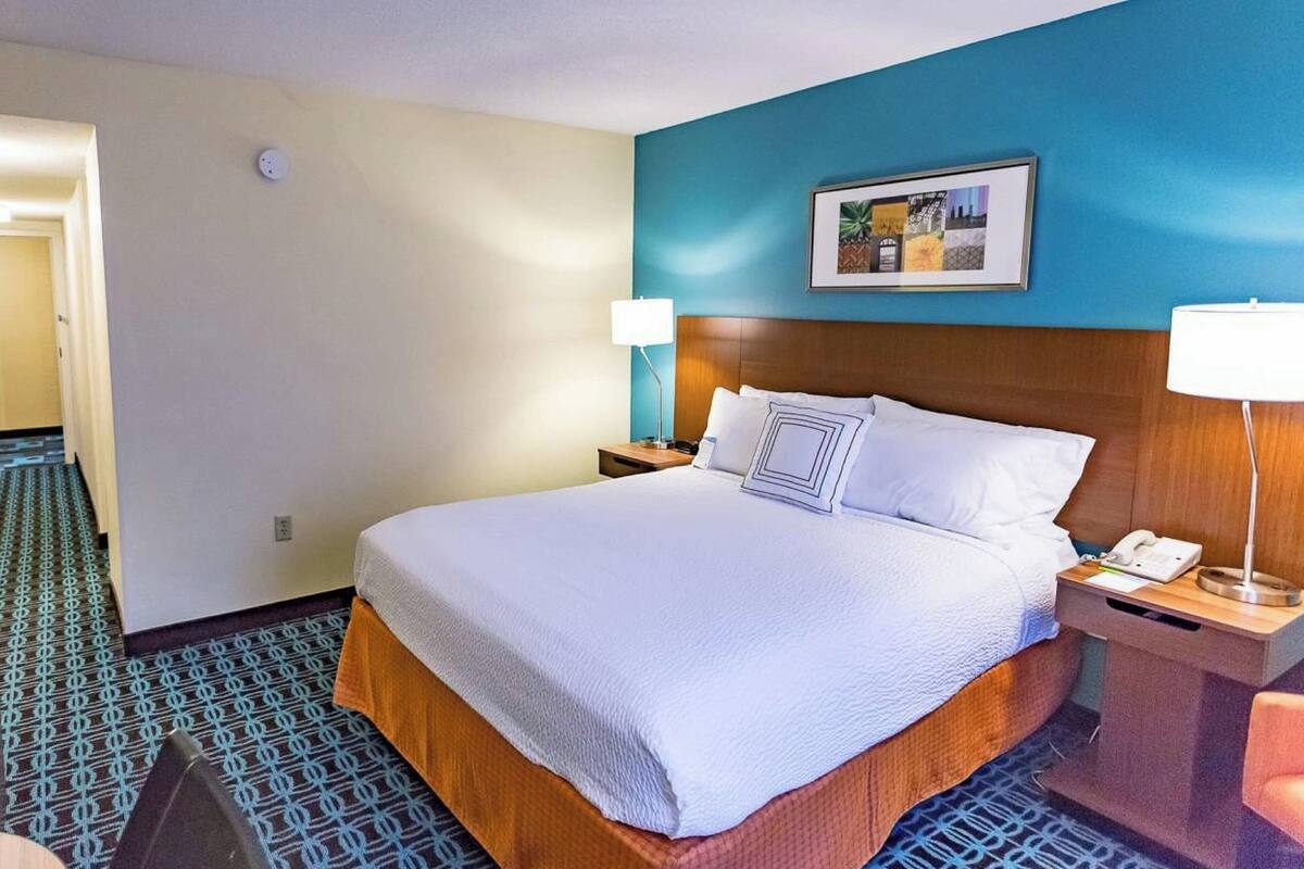 A hotel room with a large bed, two bedside tables with lamps, a framed picture on the wall, and a patterned carpet.