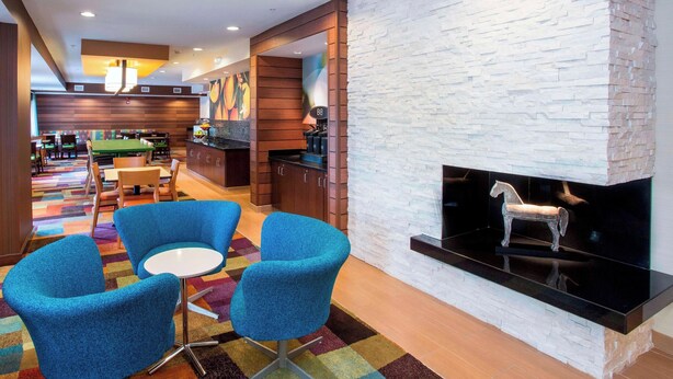 A modern lounge area with blue chairs, a billiards table, and a fireplace with a decorative horse sculpture. - Fairfield Inn & Suites Dayton South (Dayton)