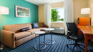 A hotel room with a teal wall, a brown sofa, two small tables, a black office chair, and a window with curtains. - Fairfield Inn & Suites Dayton South (Dayton)