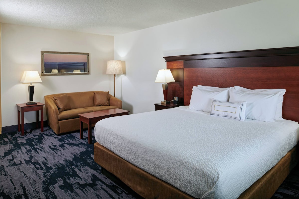 A hotel room with a large bed, a sofa, two side tables, lamps, and a framed picture on the wall.