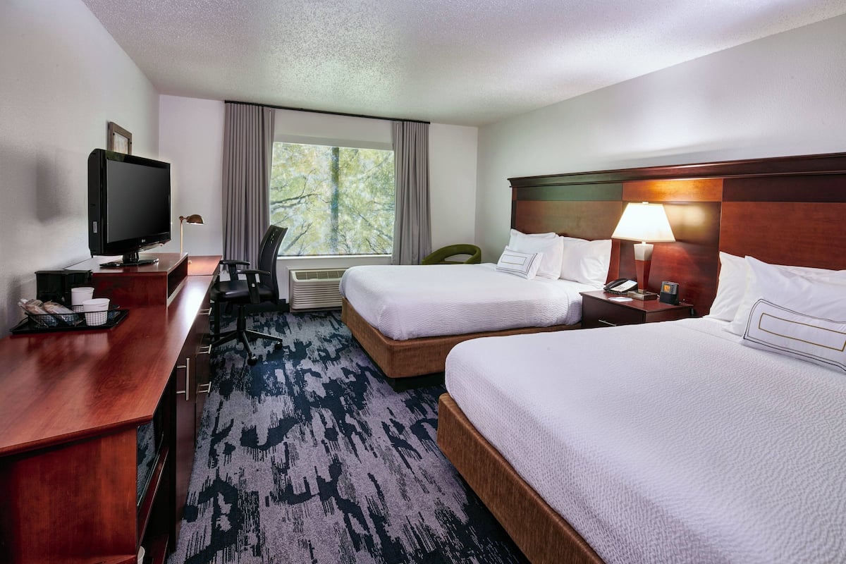 A hotel room with two beds, a desk with a television, a chair, and a window with curtains.