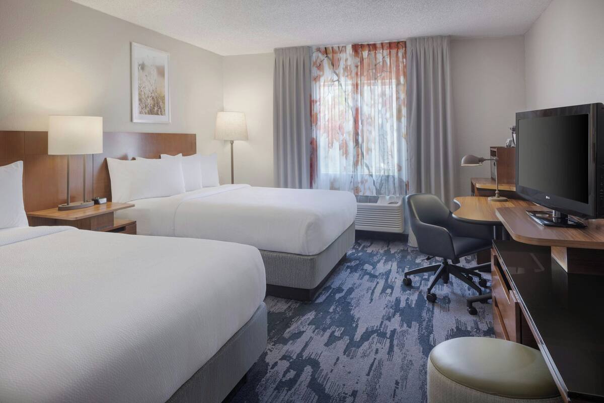 A hotel room with two beds, a desk with a computer, a TV, and a chair.
