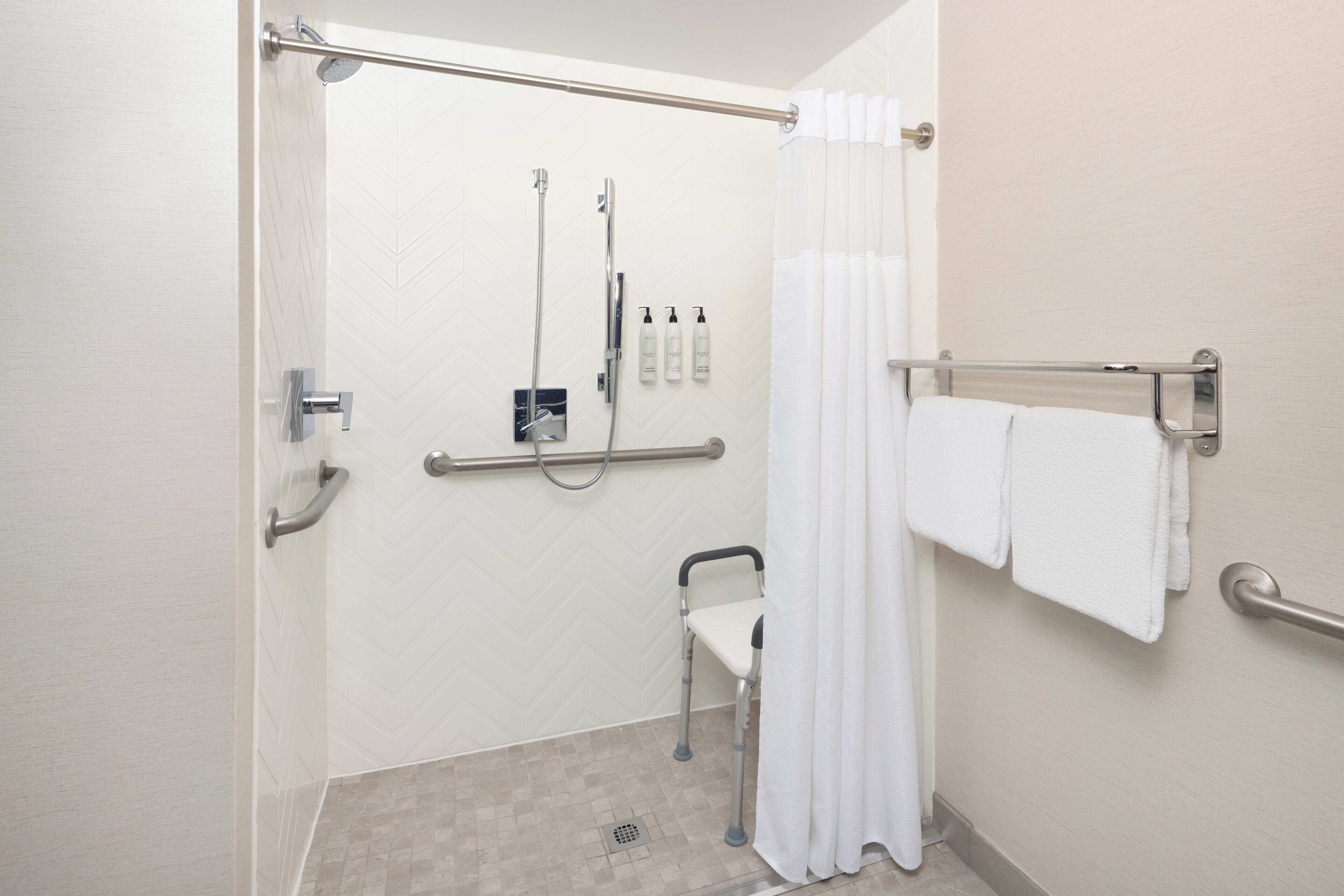 A handicap-accessible shower area with a grab bar, a showerhead, and a towel rack with towels.