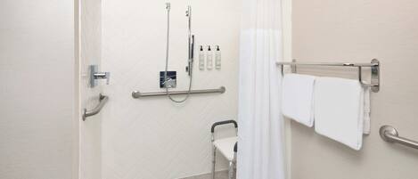 Zona de ducha accesible para personas con movilidad reducida, con barra de apoyo, cabezal de ducha y toallero con toallas.