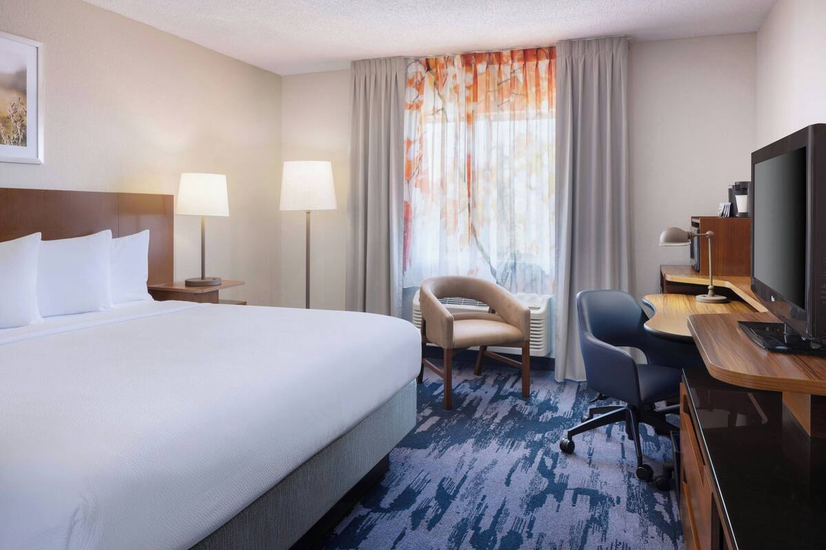 A hotel room with a large bed, two bedside lamps, a desk with a computer, a chair, and a television.