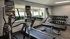 A gym with treadmills, an elliptical, and a bench press. There are dumbbells on a rack and a TV mounted on the wall. - Fairfield Inn & Suites Jacksonville Airport (Jacksonville)