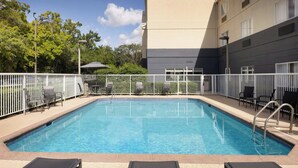 A rectangular swimming pool with a white fence, surrounded by lounge chairs and a building with a beige exterior. - Fairfield Inn & Suites Jacksonville Airport (Jacksonville)