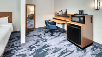 Una habitación de hotel con cama, escritorio, silla, microondas y refrigerador.