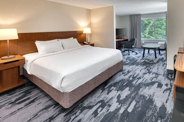 A hotel room with a large bed, two bedside tables with lamps, a desk with a chair, and a large window with a view of trees.