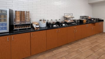 Una barra de desayuno con diversas opciones de comida, como avena y bollería, además de una máquina de café.