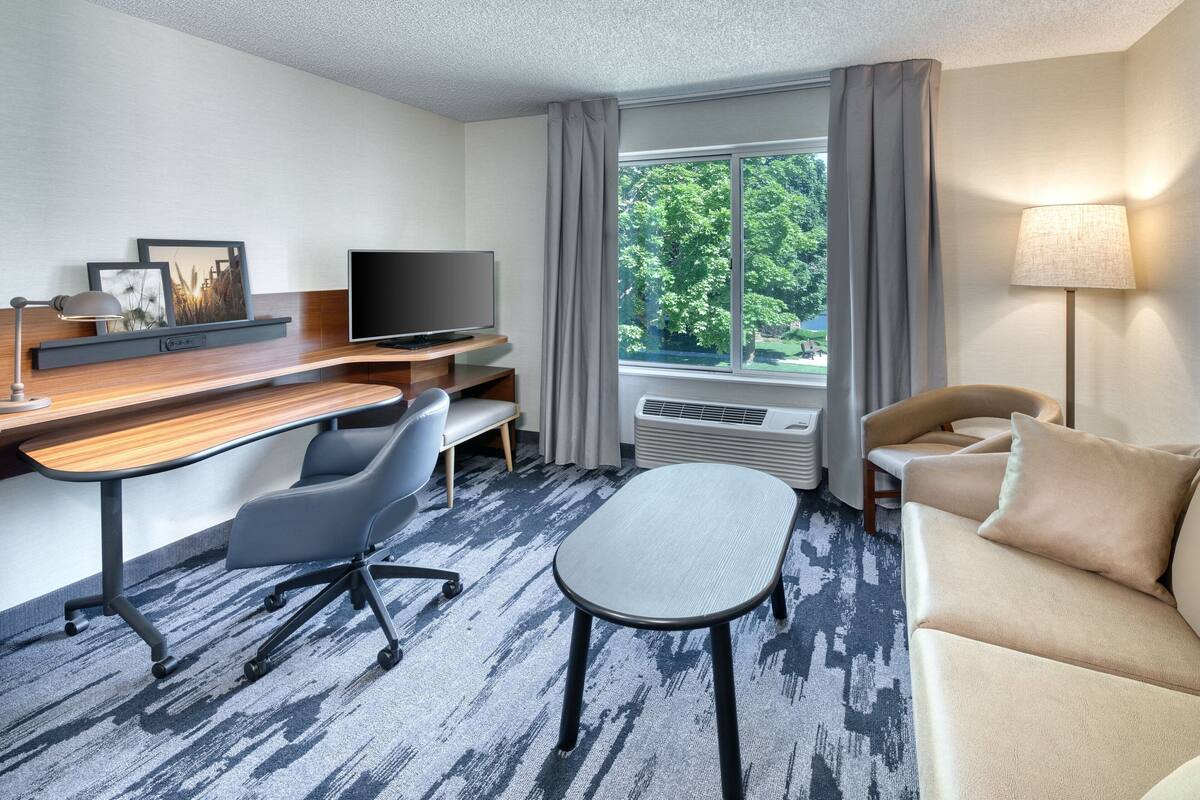 A hotel room with a desk, a TV, a sofa, and a window with curtains.