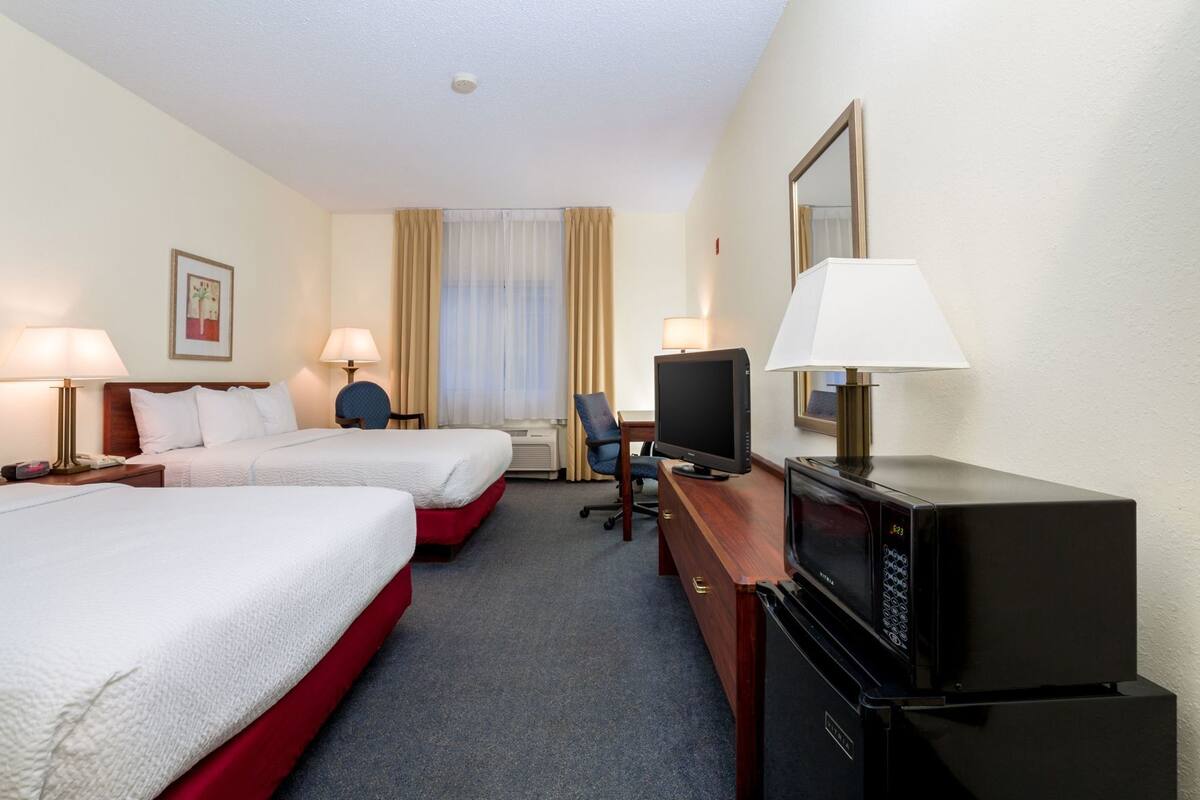 Ein Hotelzimmer mit zwei Betten, einem Schreibtisch mit Fernseher, einem Sessel und einer Schreibtischlampe.