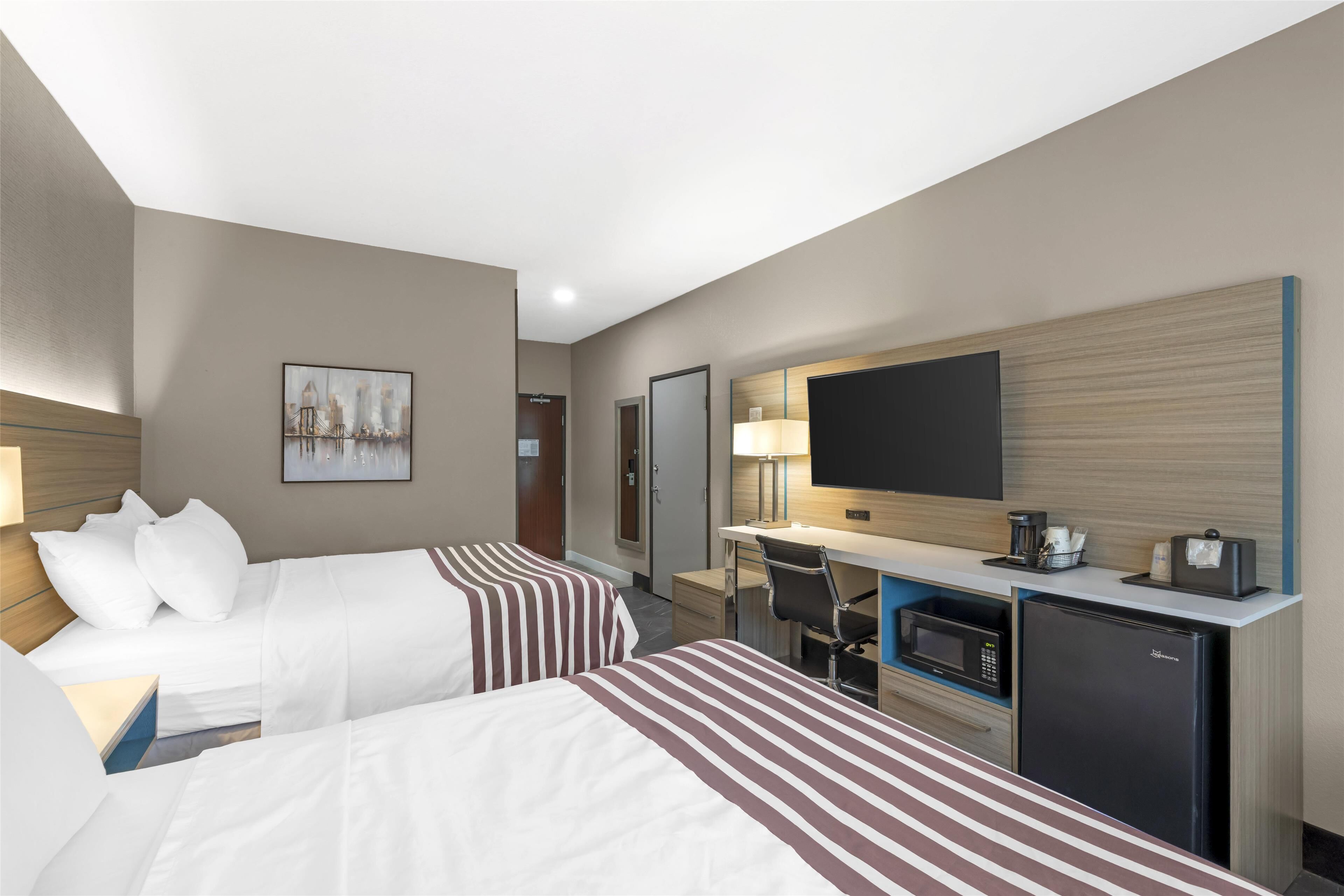 A hotel room with two beds, a desk with a computer, a television, and a refrigerator.