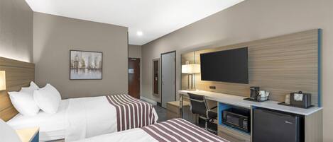 A hotel room with two beds, a desk with a computer, a television, and a refrigerator.