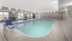 Une piscine intérieure avec une chaise bleue, une échelle et un sol carrelé.