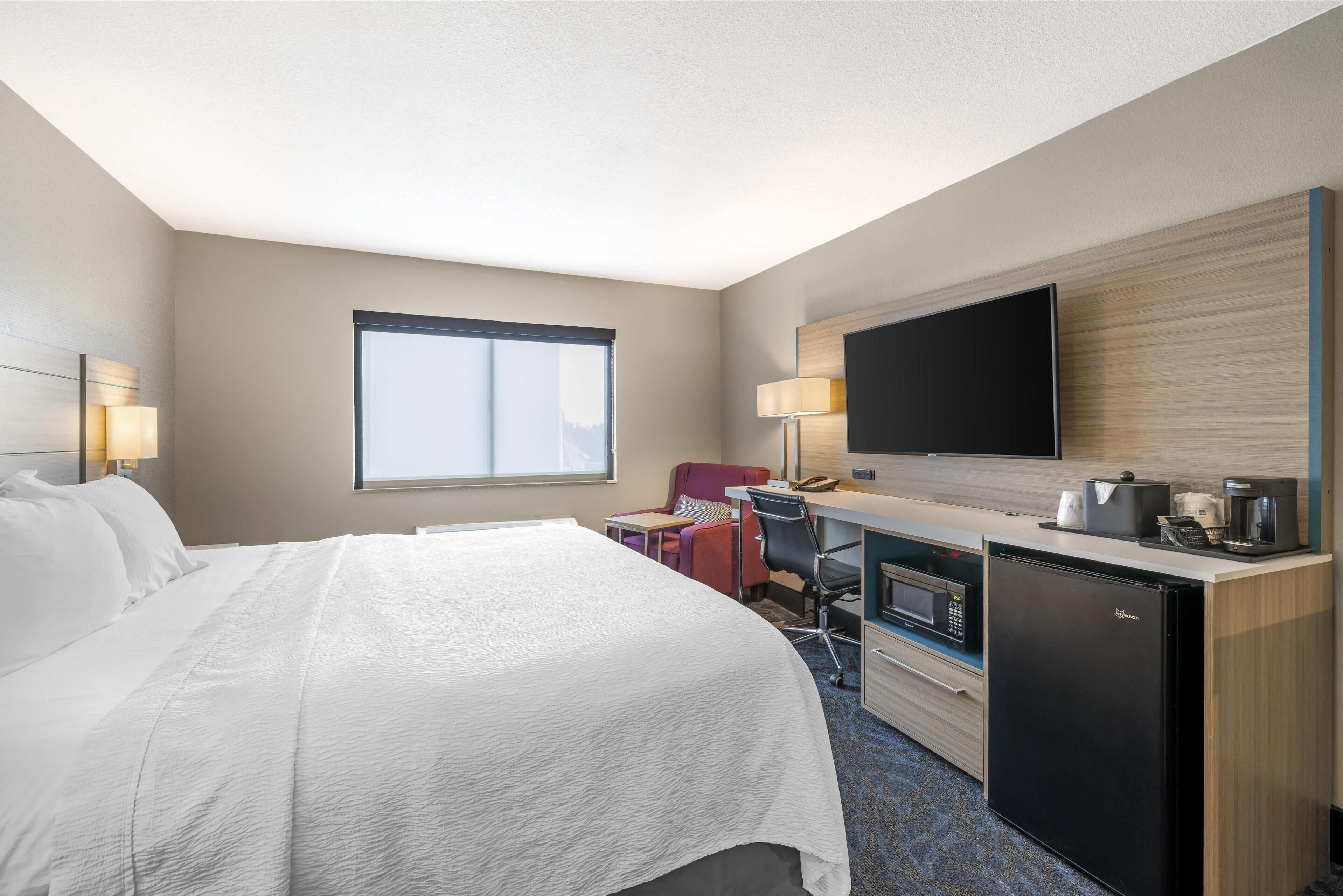 A hotel room with a bed, desk, chair, television, and a refrigerator.