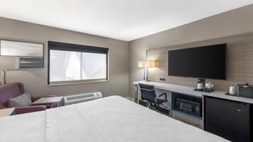 A hotel room with a bed, a desk with a computer, a flat-screen TV, a microwave, and a refrigerator.