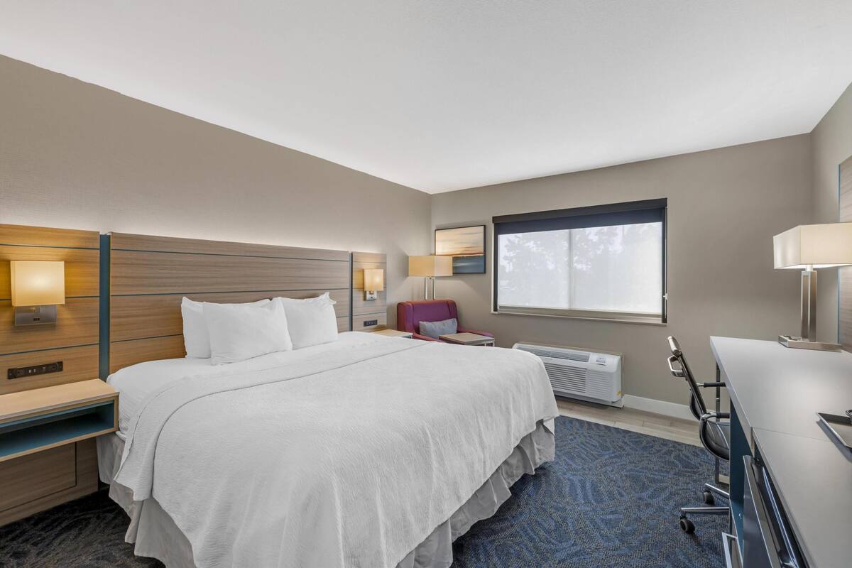 Ein Hotelzimmer mit einem großen Bett, einem Schreibtisch, einem Stuhl und einem Fenster.