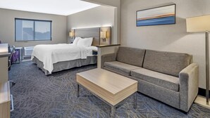 Une chambre d’hôtel comprenant un lit, un canapé, une table basse, un bureau avec une chaise et une grande fenêtre.